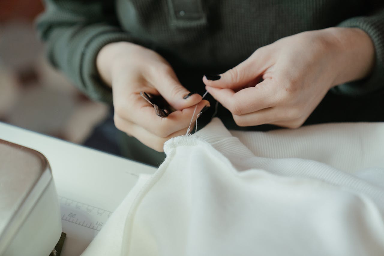 Close-up of hands sewing fabric with a needle and thread, showcasing careful craftsmanship.