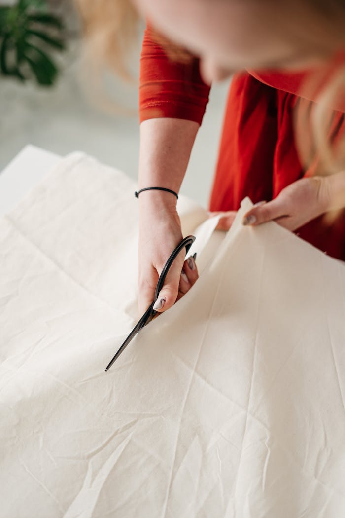 Focused seamstress cutting white cotton fabric with scissors, showcasing zero waste fashion.