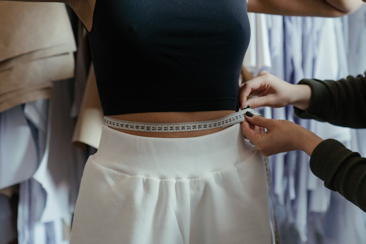 Detailed view of a tailor measuring a clients waist in a clothing workshop, focusing on precision.